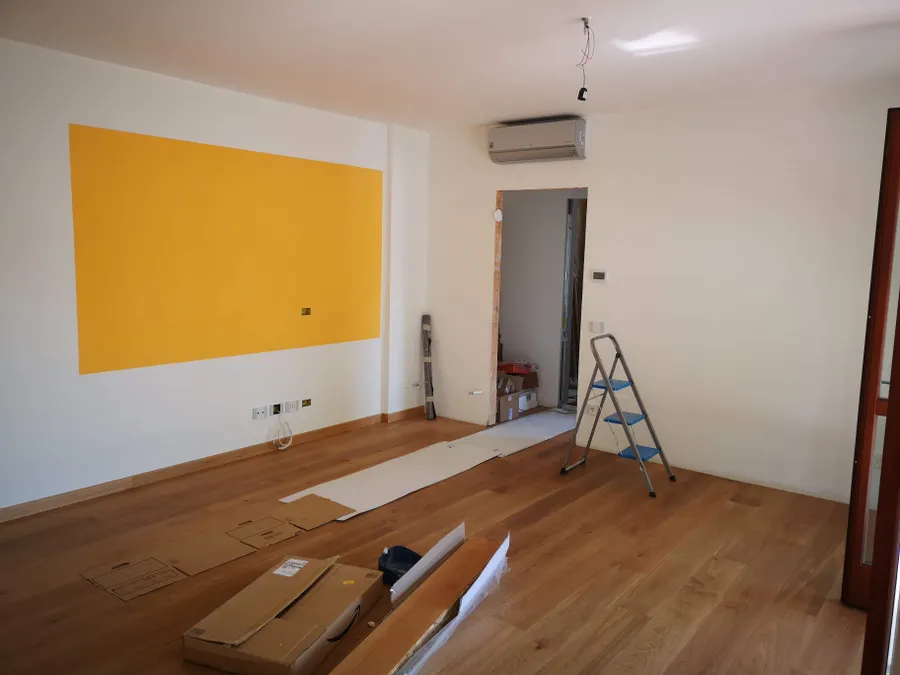 Empty renovation room with white and yellow walls, a stepladder and cardboard protection on wood flooring